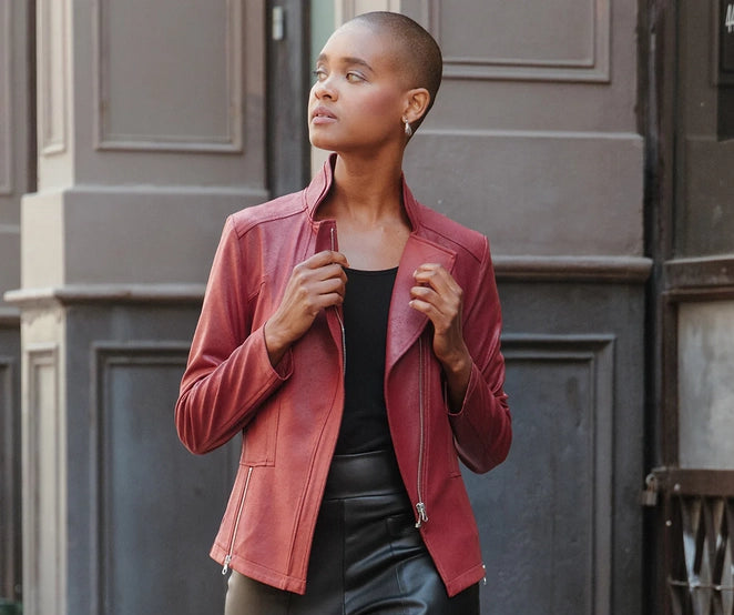 Woman wearing a red vegan leather jacket and black leather pants standing against a gray wall.